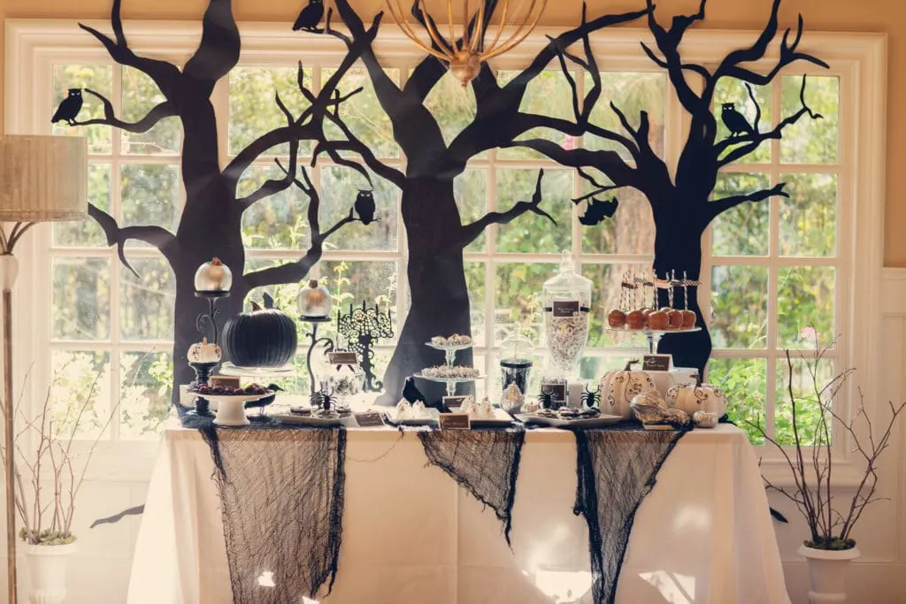 DIY Halloween party decorations of black silhouettes of trees with no leaves and owls and bats on the trees behind the serving table.