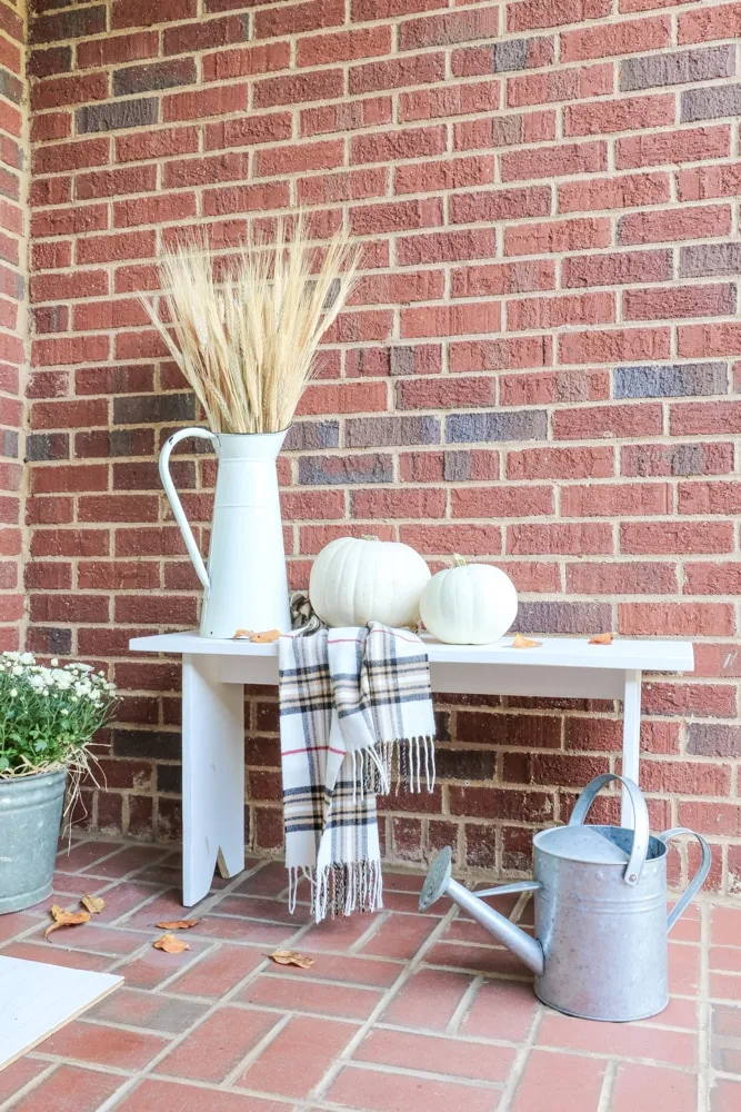 Fall front porch accessories of pumpkins, scarf, and french pitcher filled with wheat