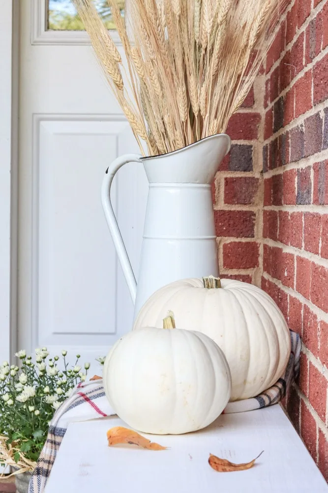 White pumpkins sitting on a farmhouse bench on a tiny front porch for autumn