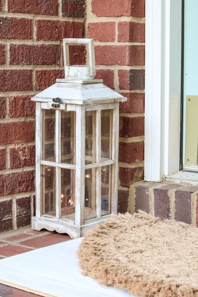 Small front porch decor using a painted lantern with mini lights inside.