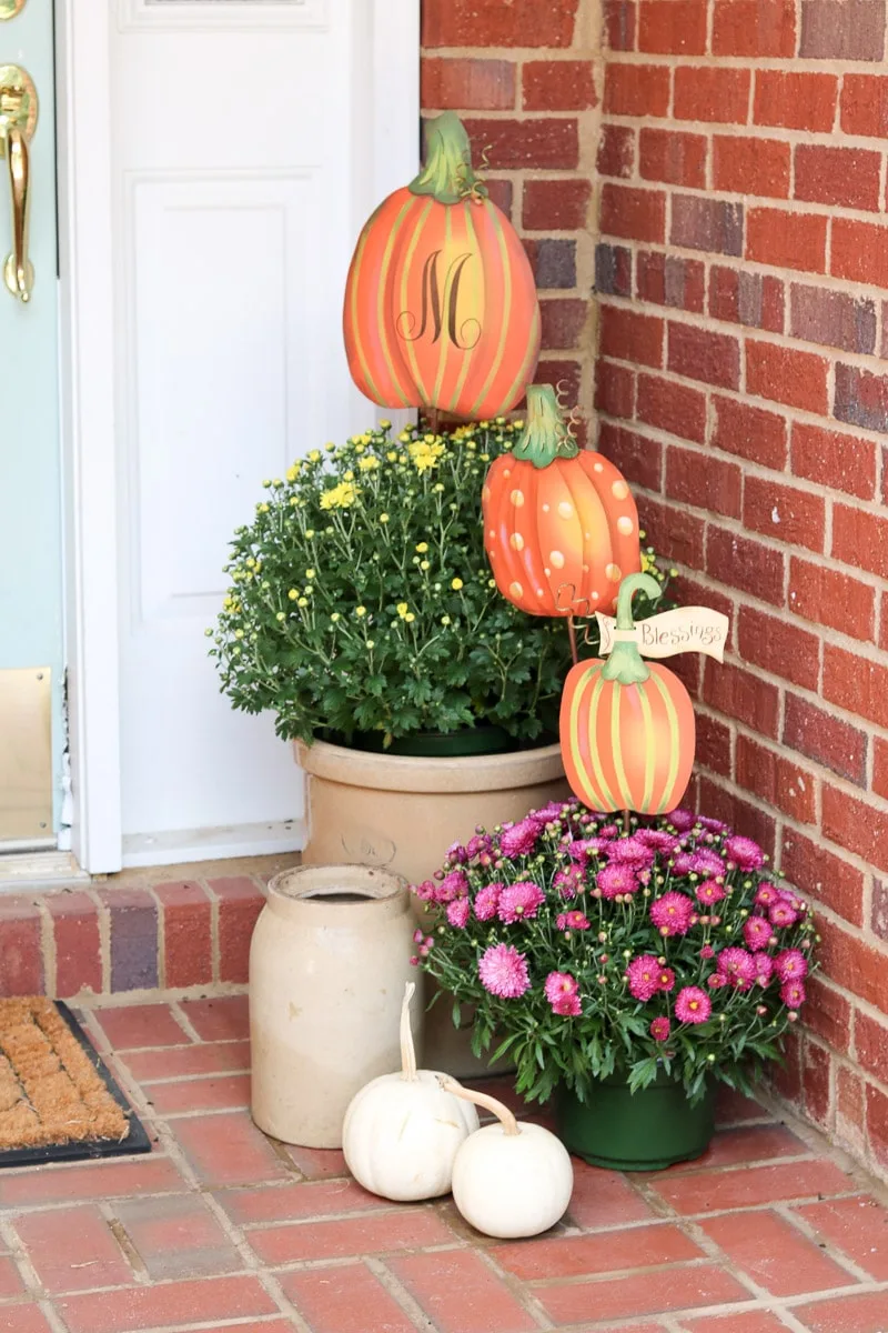 Fall decorations for a small front porch using crocks, small white pumpkins, mums and pumpkins metal signs.
