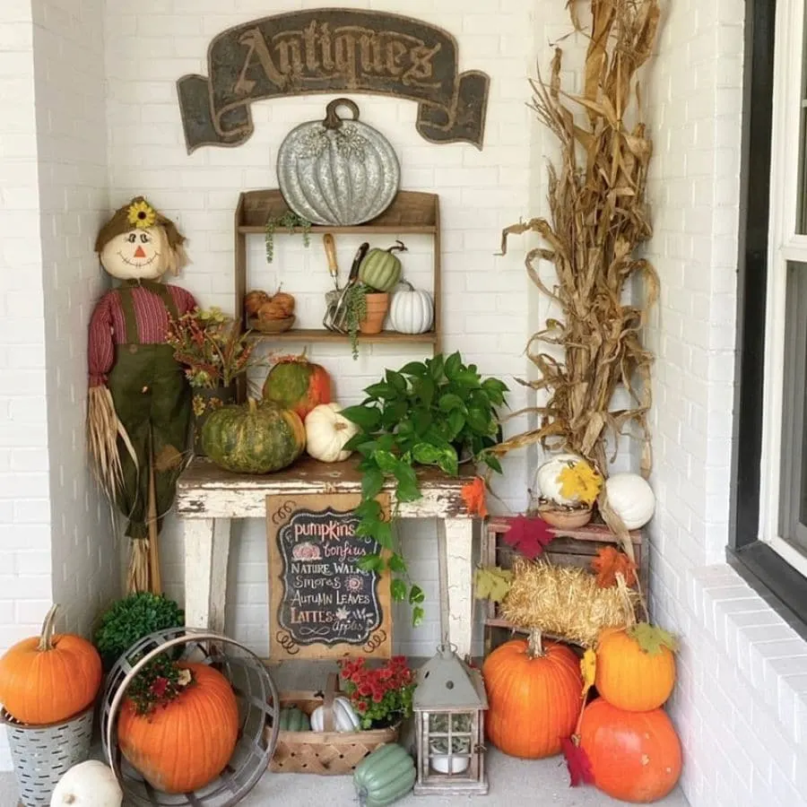 A fall styled nook on a front porch filled with decorations like pumpkins and a scarecrow.