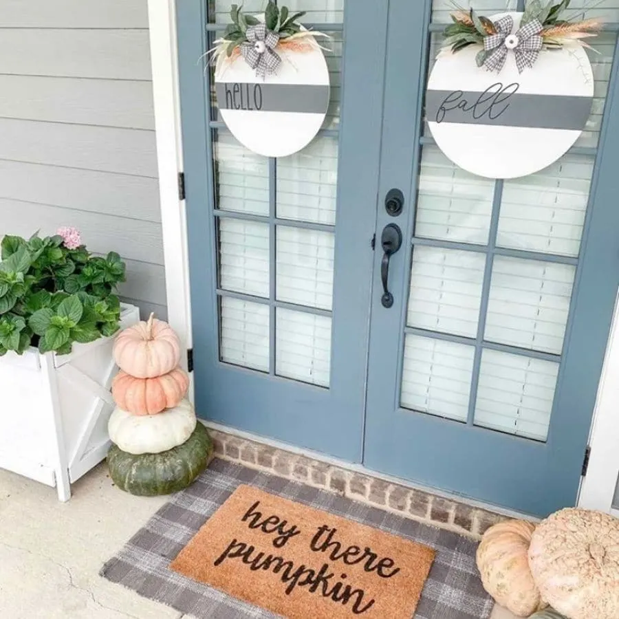 Another fall front door decor with layered mats and stacked pumpkins.