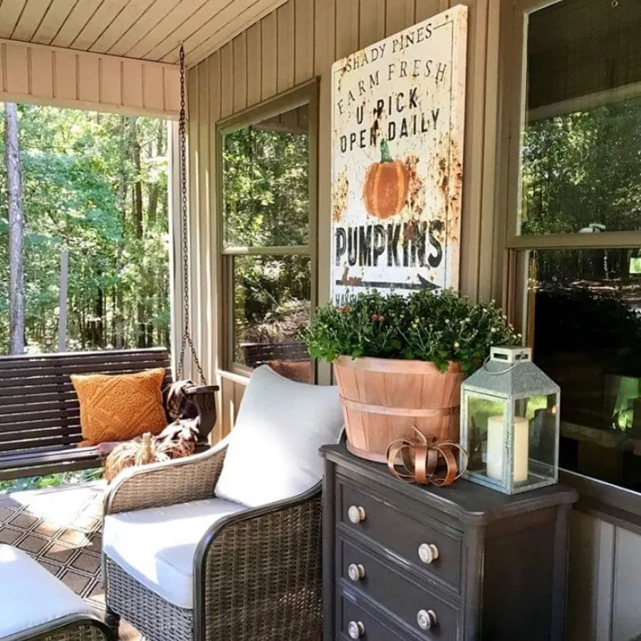 A fall front porch with a vintage pumpkin farm sign hanging on the wall.