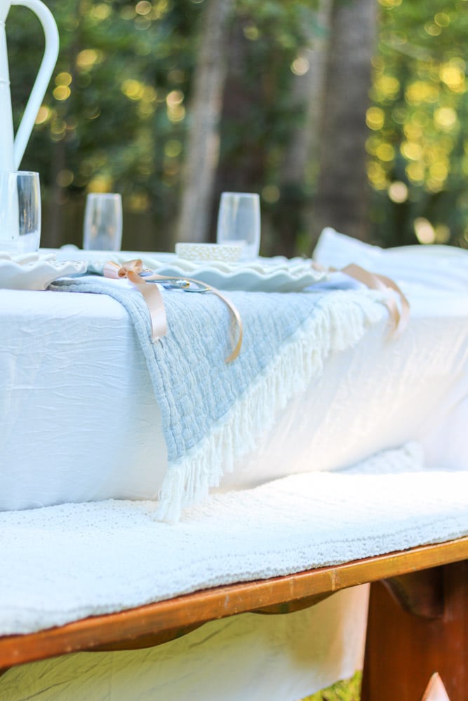Tablescape for fall showing a white tablecloth with a blue blanket with white fringe acting as a table runner.