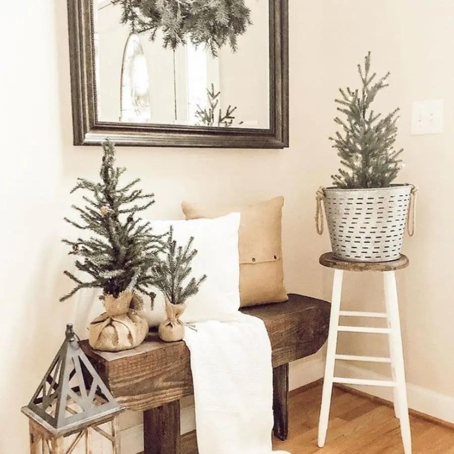 A pretty wooden bench with pillows a blanket and a few mini trees on it, perfect for Christmas.