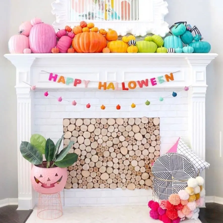 Pumpkins painted in rainbow color sitting on a white fireplace mantle.  Happy Halloween garland hanging on front of the mantle.