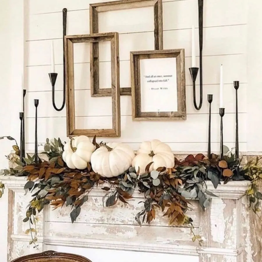 Greenery on a chippy mantle with white pumpkins sitting on top and black candle sticks on the ends.