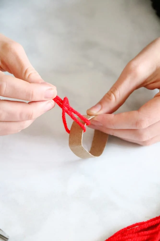 Tie pieces of red yarn to a toilet paper roll to make a winter hat garland