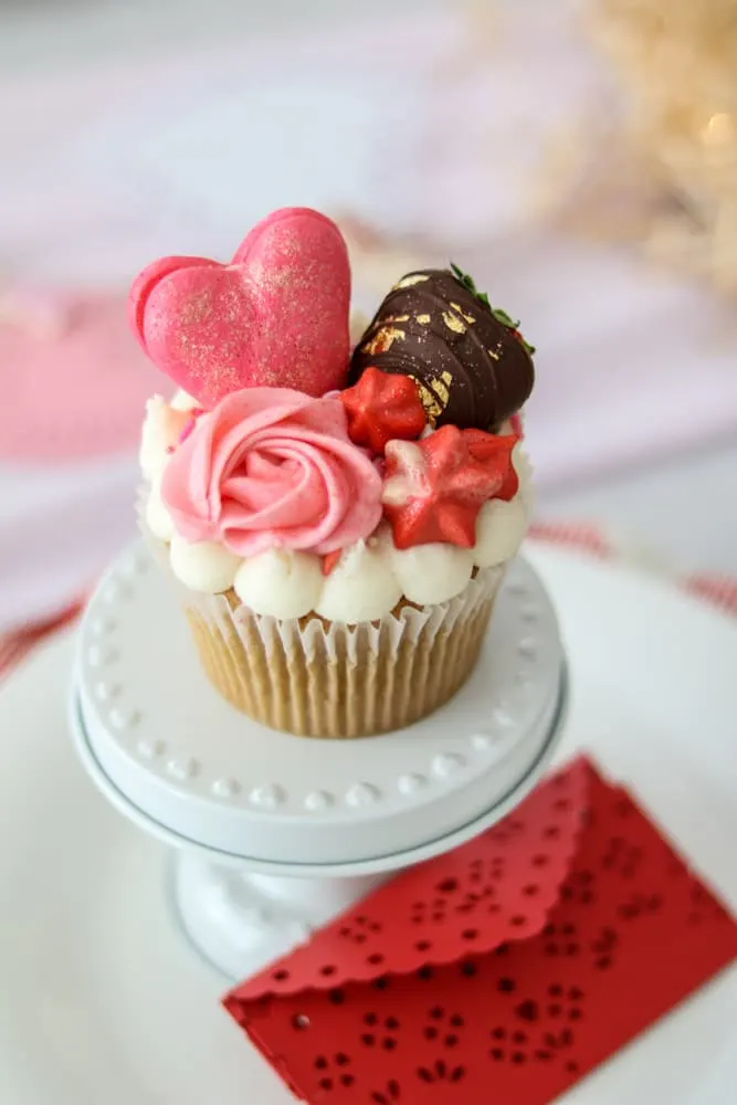 Les Cherie beautiful large cupcake with light pink icing rose, red stars, chocolate covered strawberry with gold foil and pink heart shape macaroon dusted with glitter.  Gluten and dairy free