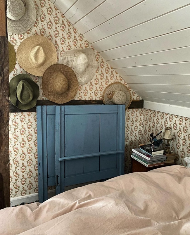 Cottagecore room ideas like this bedroom with a beautiful blue door and hats on the wall