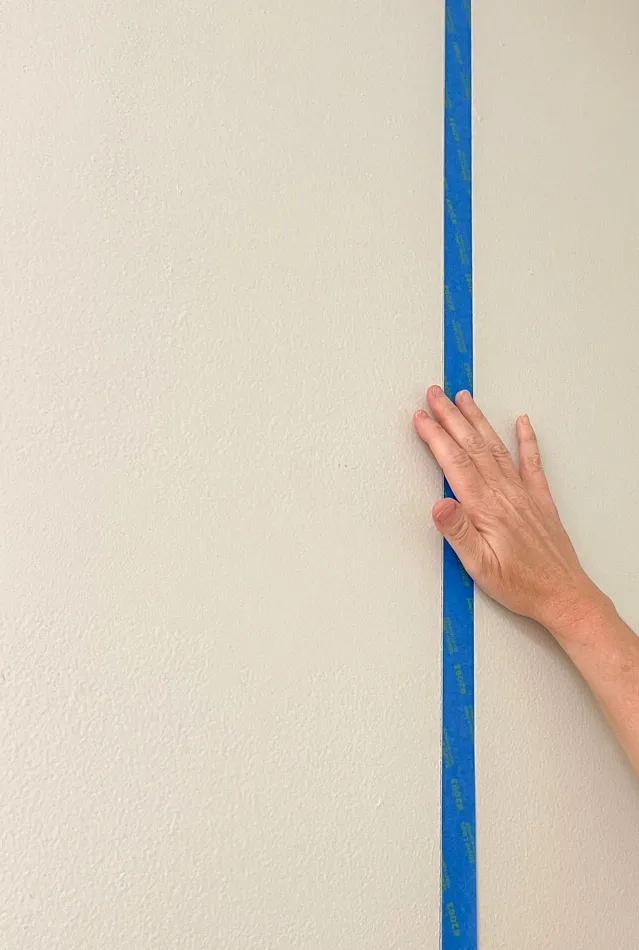 Placing painters tape on the wall to paint the background of this DIY mud room storage unit.