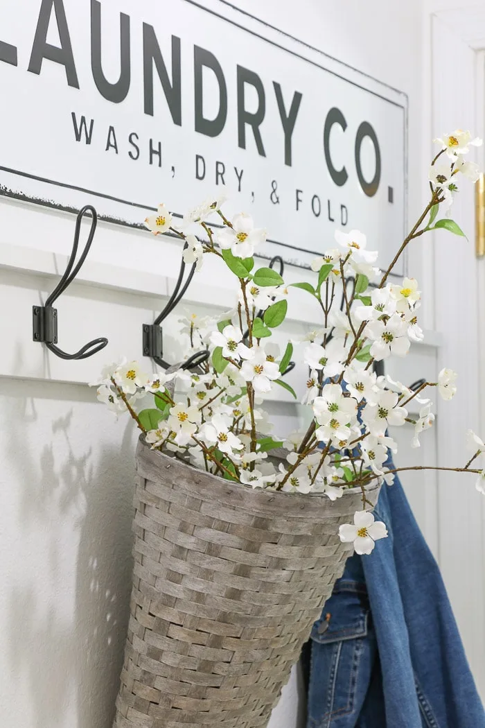 Tiny laundry room converted into a mudroom laundry room by adding a wooden coat rack to wall to hand coats and baskets and then decorated with a metal laundry sign.