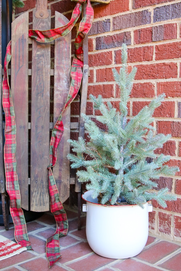 Small Christmas tree nestled next to a old sled on a Christmas decorated front porch