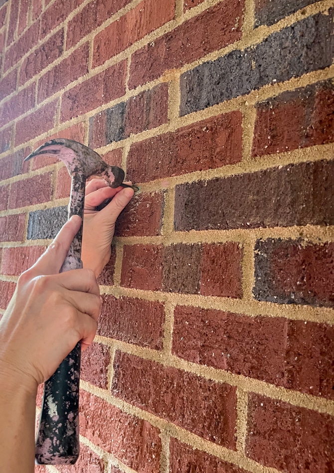 Hammering a steel case nail into brick mortar to hang a wreath