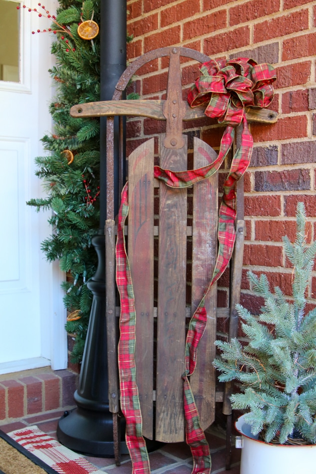 Old fashioned sled with plaid ribbon on a cottage farmhouse Christmas porch