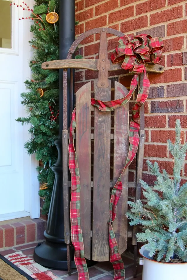 Old fashioned sled with plaid ribbon on a cottage farmhouse Christmas porch