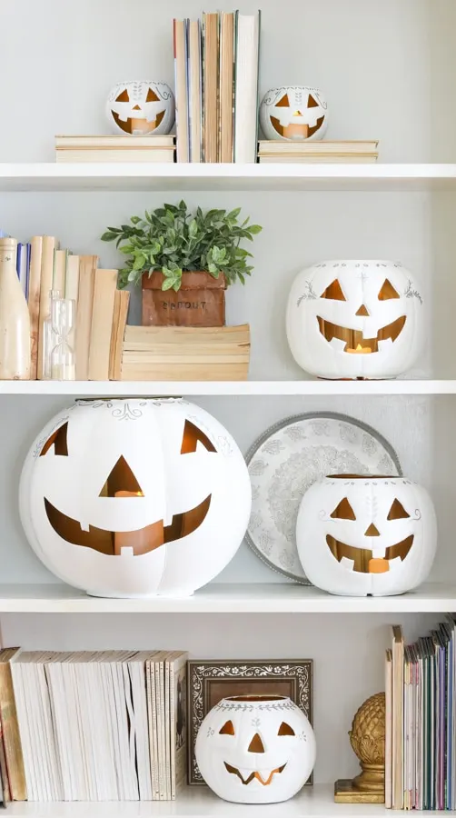 White chalk painted dollar store pumpkins with a face on bookcase