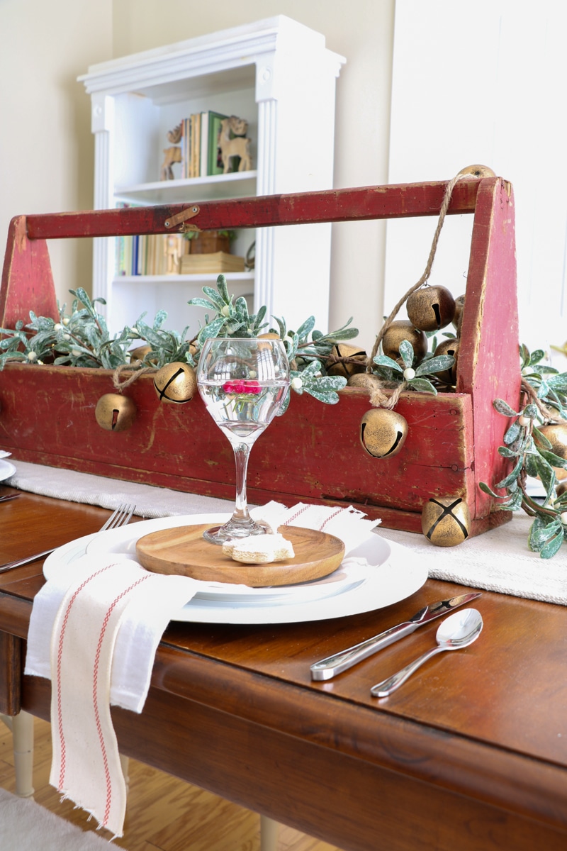 Table setting with antique tool box in red patina color.  Filled with frosted mistletoe garland, antique gold jingle bells and fairy lights