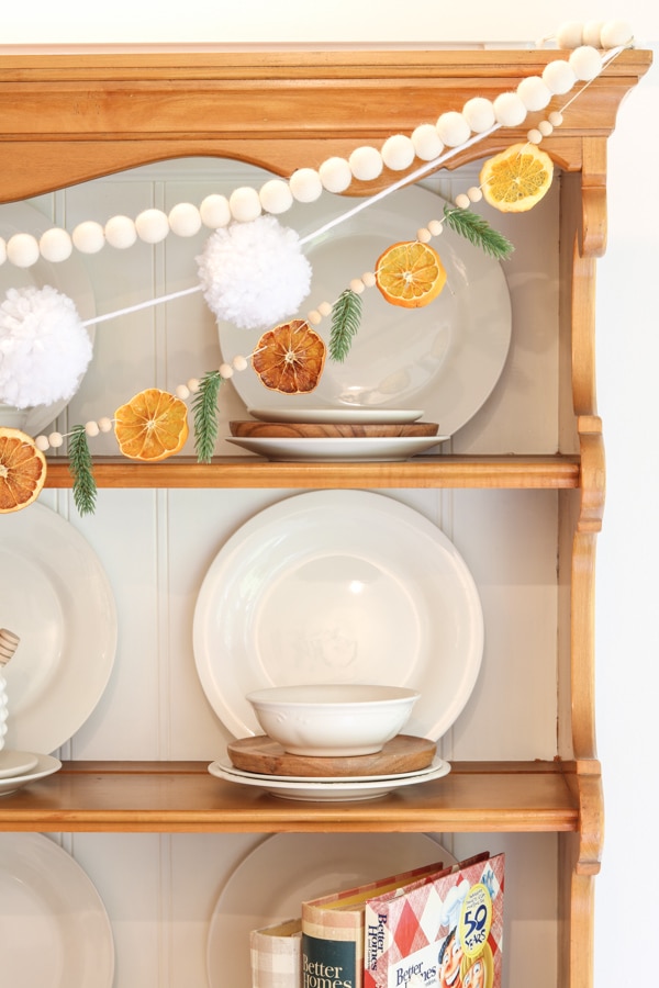 DIY dried orange garland with fir sprigs and wood beads swagged across a wooden hutch