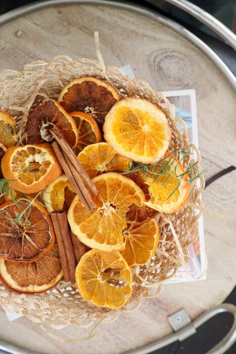Overhead view of dried orange slices, cinnamon sticks, and rosemary in a woven basket