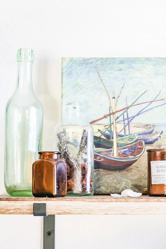 Vintage bottles and jars in front of a sea oil painting sitting on shelves
