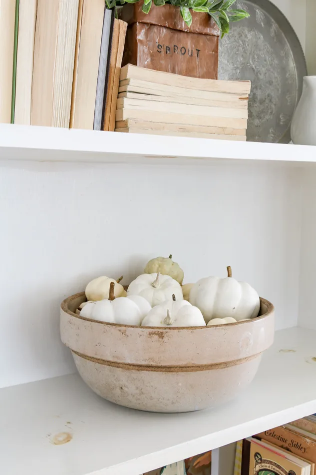 White pumpkins added to a crock bowl for decorations on a bookcase for fall