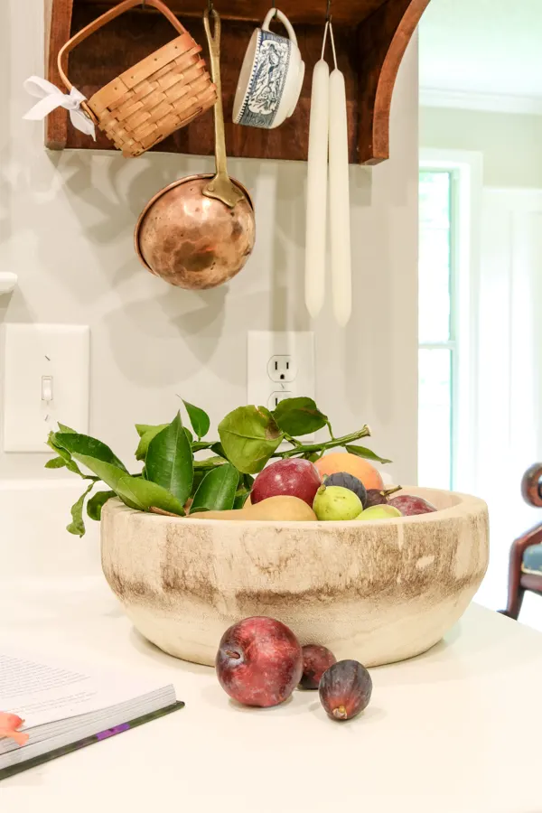 Fruit in a wooden bowl and vintage accessories hanging from homemade plate rack