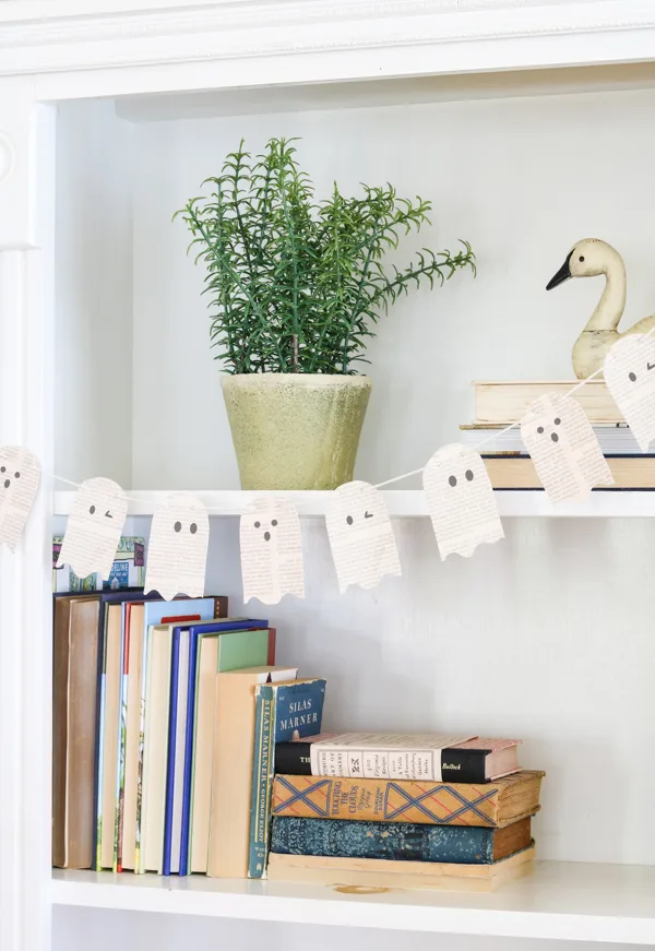 Printable book page ghosts garland craft set.  This ghost garland is hanging on a bookcase as a decoration.