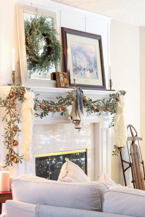 Blue Christmas color scheme mantel.  Mistltoe garland draped on front of fireplac emantel with white knit stockings on ends and white vintage ice skatesin the middle with a blue velvet bow.  Thomas Kincade winter scene art, mirror with wreath on it, tiny art in front of mirror and candles