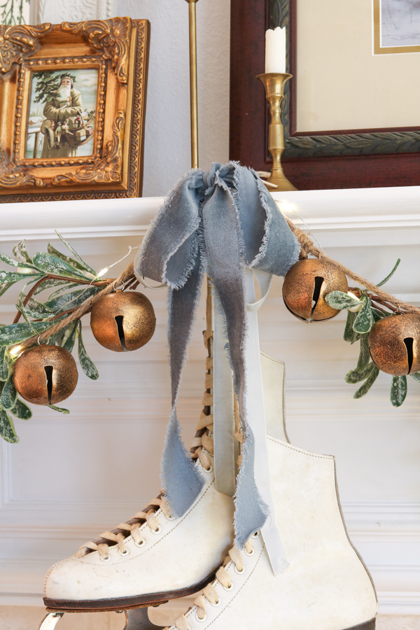 Christmas decor trends for 2025.  Vintage skates hanging on a fireplace mantel with mistletoe, jingle bells and dusty blue velvet ribbon