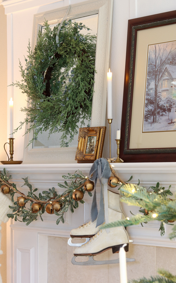 Christmas decor trends for 2025.  Vintage skates hanging on a fireplace mantel with mistletoe, jingle bells and dusty blue velvet ribbon. Mirror with wreath and candles