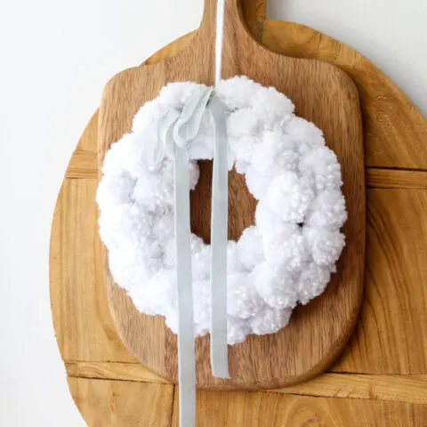 White pom pom wreath hanging on cutting boards in a kitchen