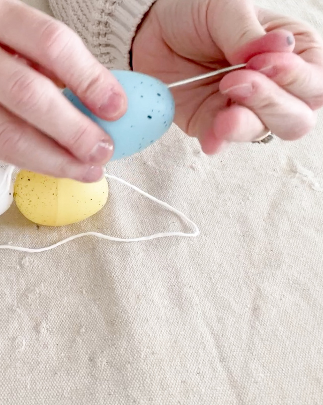 Threading twine through a plastic easter egg to make a garland