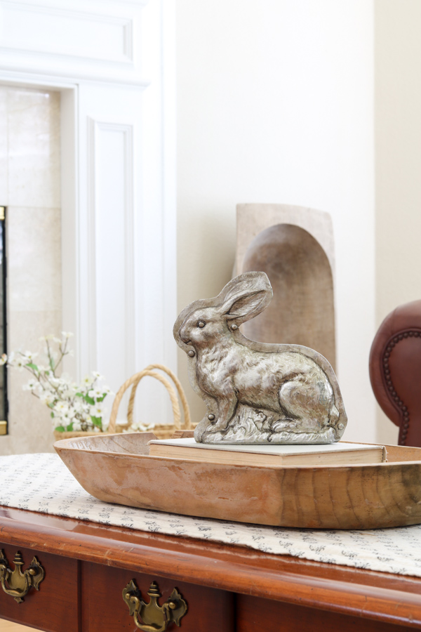 Vintage bunny mold decoration sitting on books inside a dough bowl on a coffee table for spring decorations.
