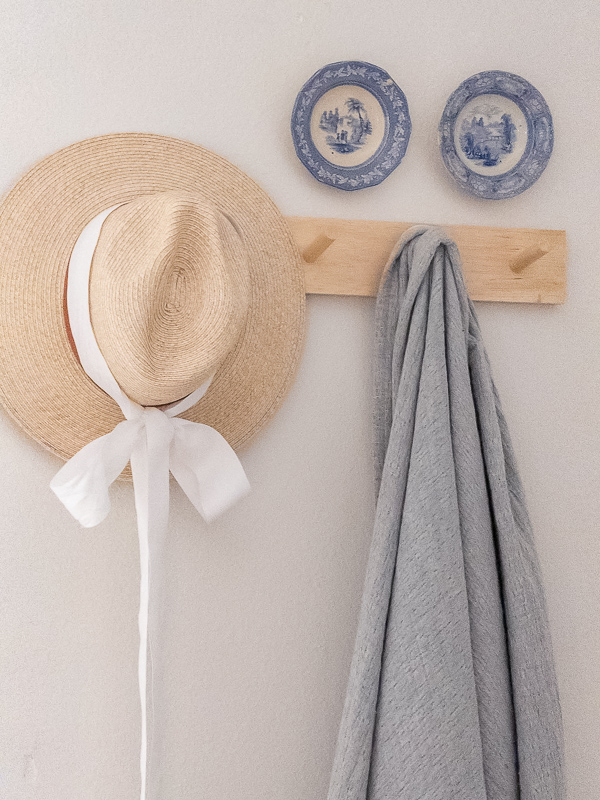 Antique blue ironstone plates hanging on a wall above a hook wtih blanket and straw hat