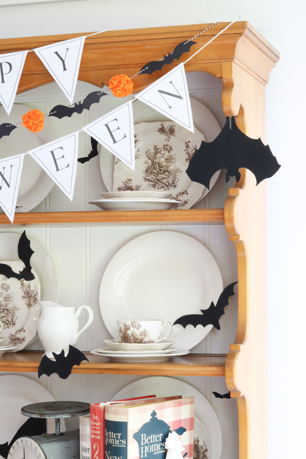 Hutch decorated for Halloween with paper.  Bat and pom pom garland, Happy Halloween pennant banner, black bat silhouettes on dishes