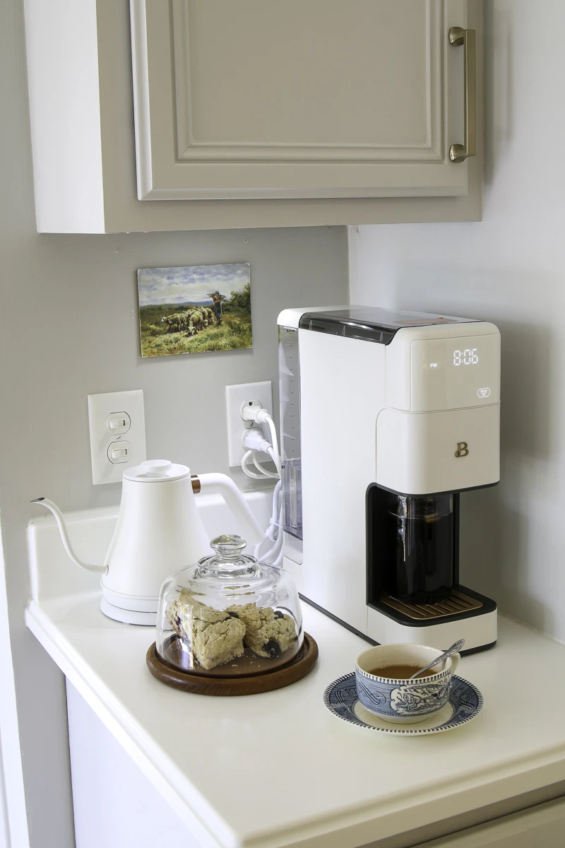 Tiny coffee bar with multifunctional coffee maker, electric tea kettle, cloche and cabinet coffee accessory storage.