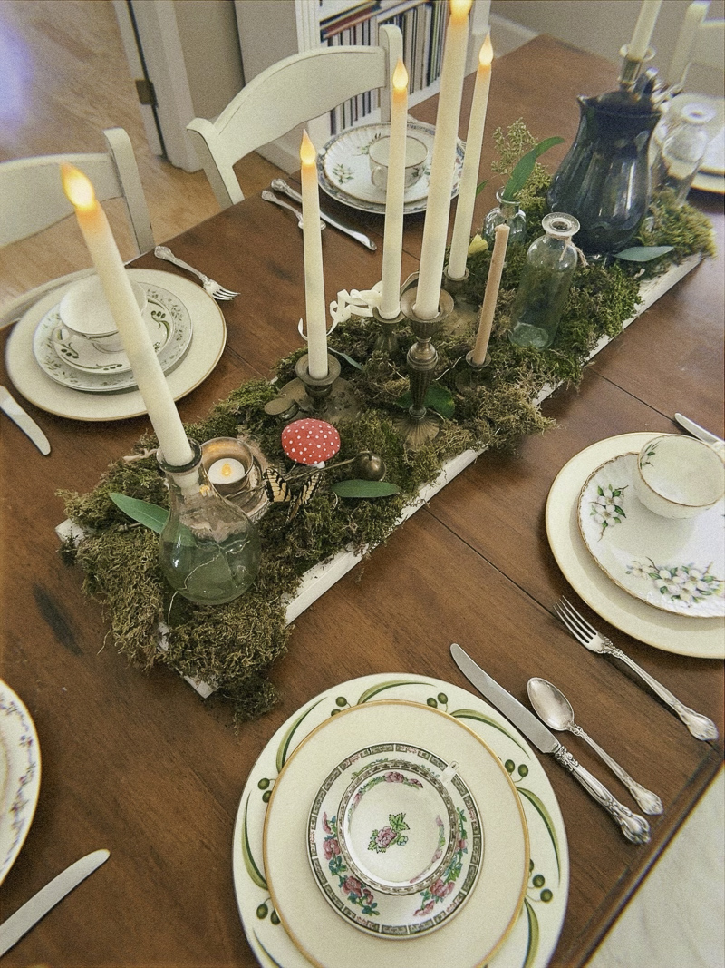 Moss centerpiece for an enchanted garden party using brass candlesticks, glass jars, silver pitcher, cups, butterflies, fairy lights and more.