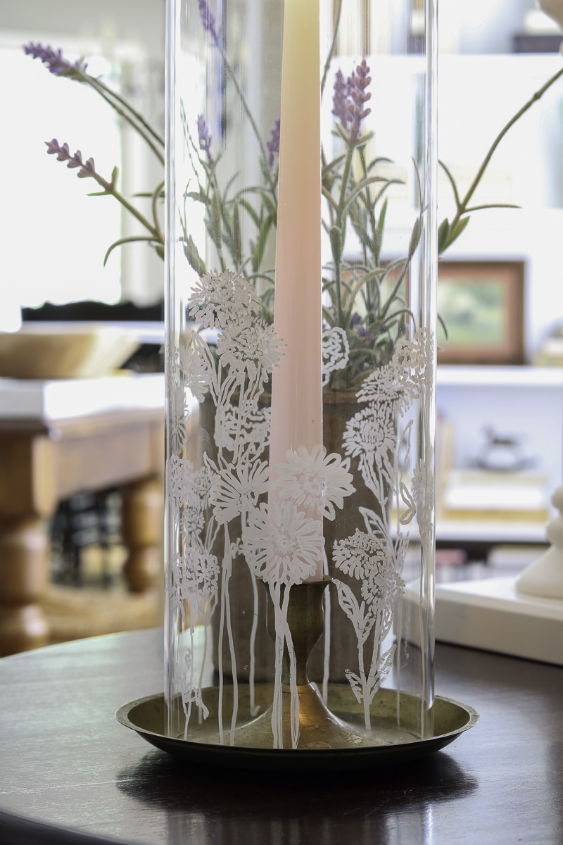 Glass cylinder with painted birth month flowers on it over a brass candle holder and taper candle