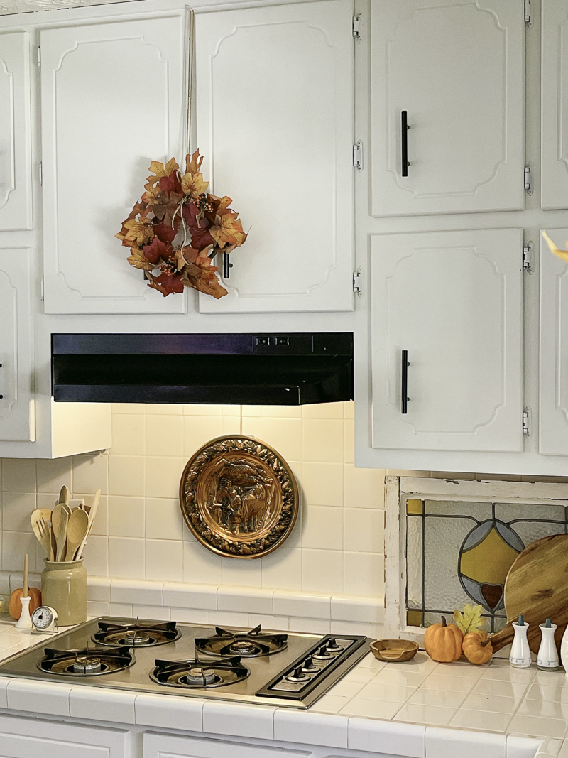 Autumn leaf wreath over range hood and copper plate decoration over stove and orange mini pumpkins.