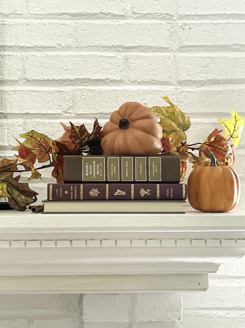 Books, pumpkins and a fall leaf garland on the mantel for autumn decorations