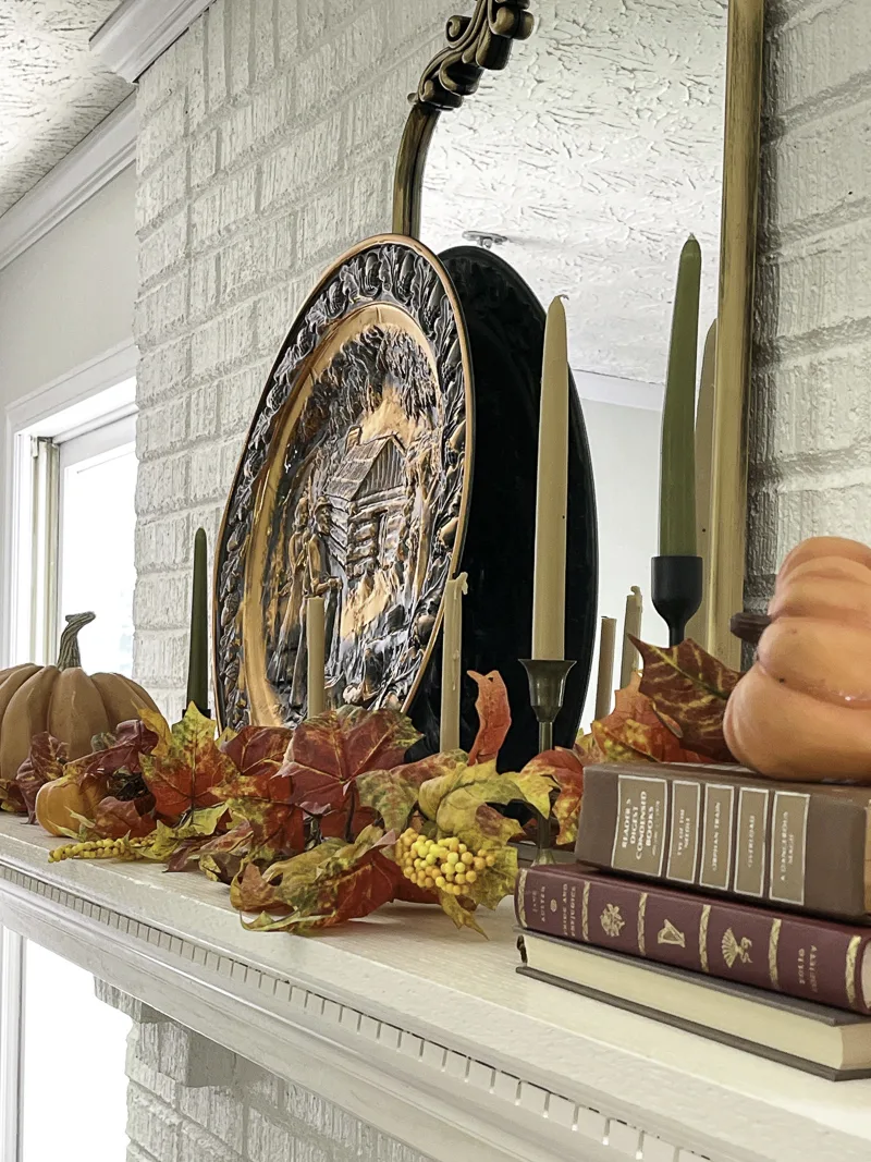 Decorating the fireplace mantel with orange and copper for fall.  Using a vintage copper platter, mirror, books pumpkins, candles and leaf garland.