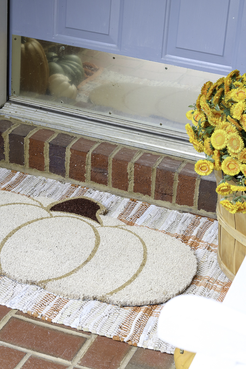 Layered rugs on a porch using a pumpkin doormat