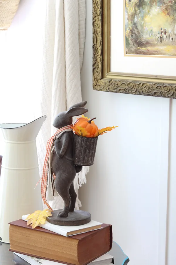 Neutral and orange fall decorations in the kitchen featuring a bunny with a basket backpack holding bright orange leaves and an orange pumpkin.