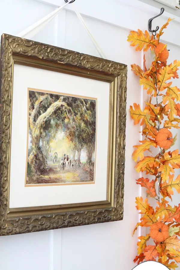 Neutral and orange fall decorations in the kitchen featuring bright orange autumn leaf garland and vintage painting.