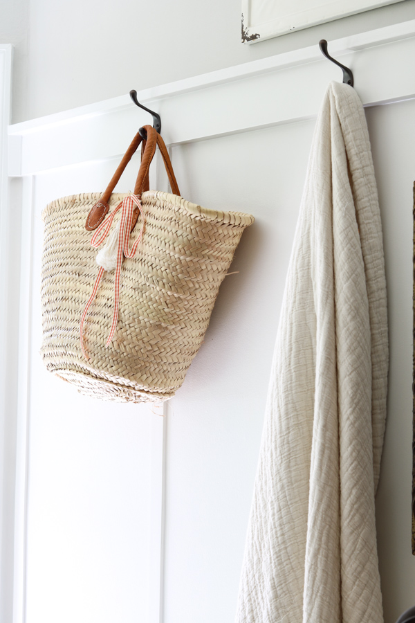 Neutral and orange fall decorations in the kitchen featuring a basket with a gingham ribbon tied on it and a cozy neutral blanket hanging on a hook.