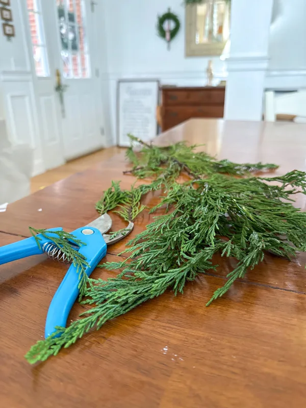 Trim small branches of greenery to decorate a Christmas candle hoop wreath