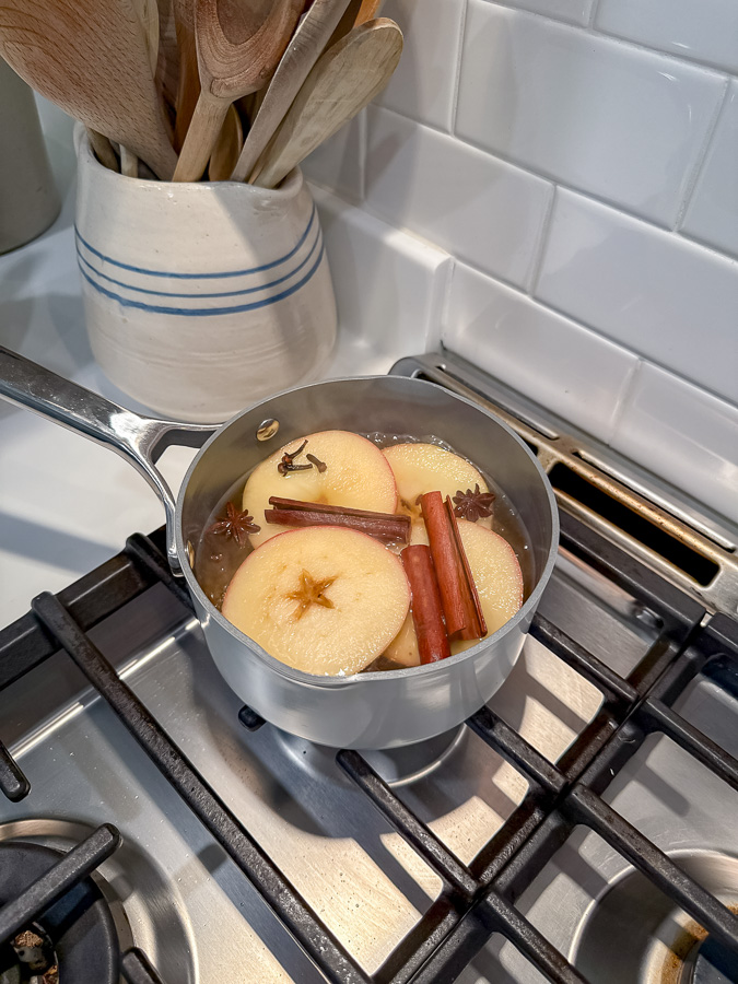 Apple pie simmer pot ingredients coming to a boil.  Inside the pot is sliced apples, whole cloves, cinnamon sticks and star anise.