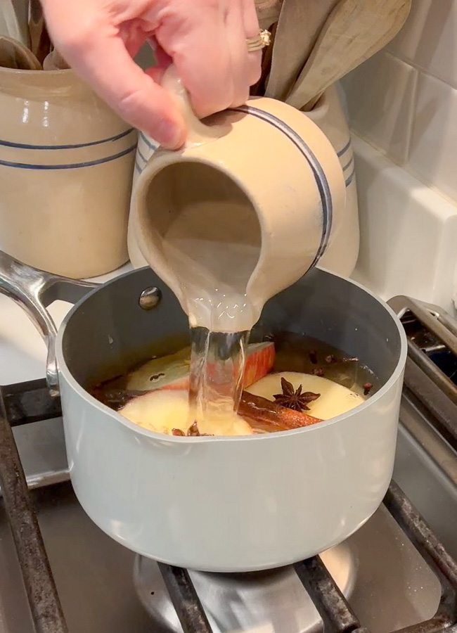 Adding what to a simmer pot filled with apple pie scent ingredients.